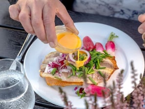Una persona versa una salsa gialla su un piatto con pesce, ravanelli e cipollotti.