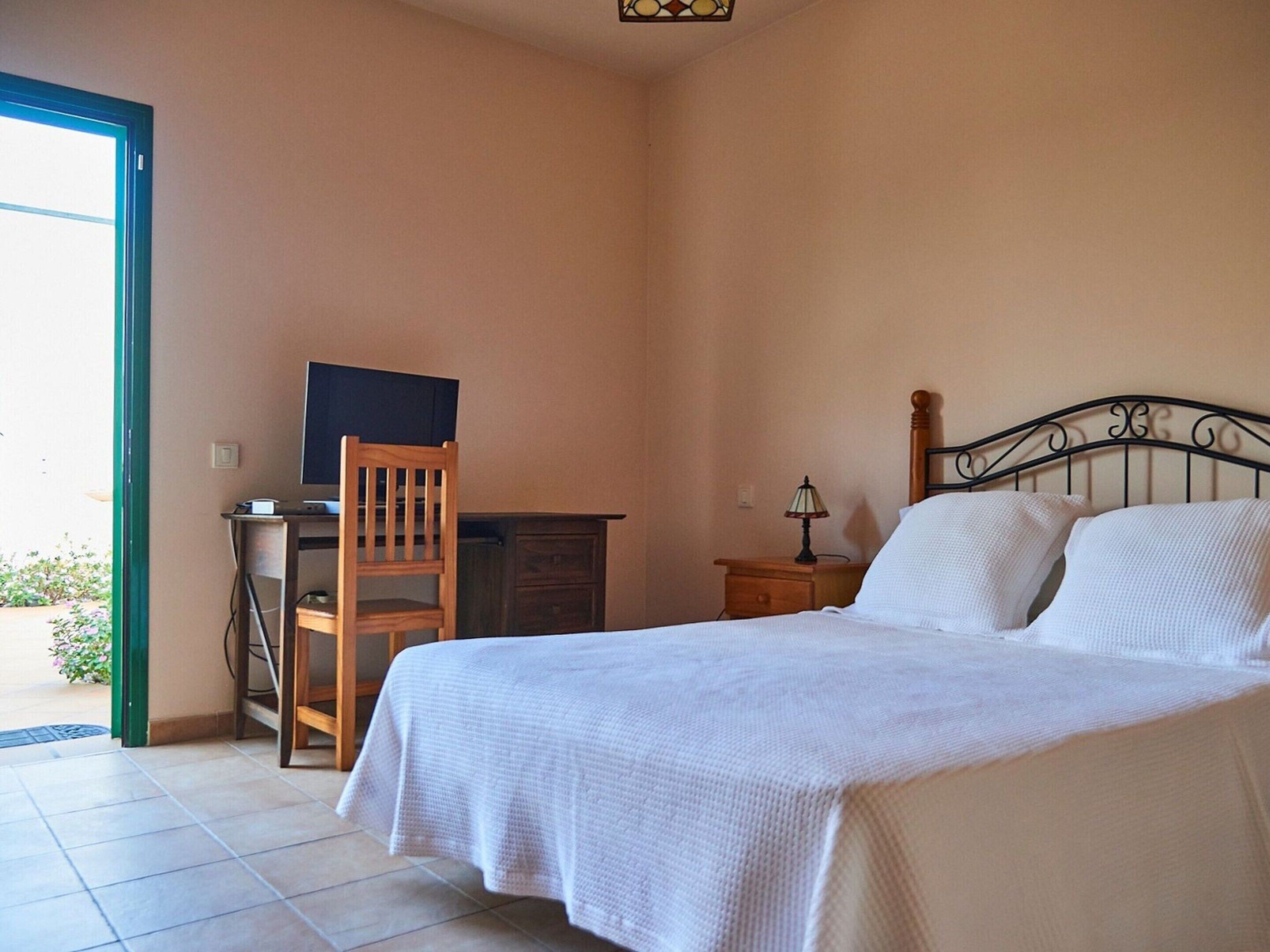 A bedroom with a bed, a desk, a chair, and a television.