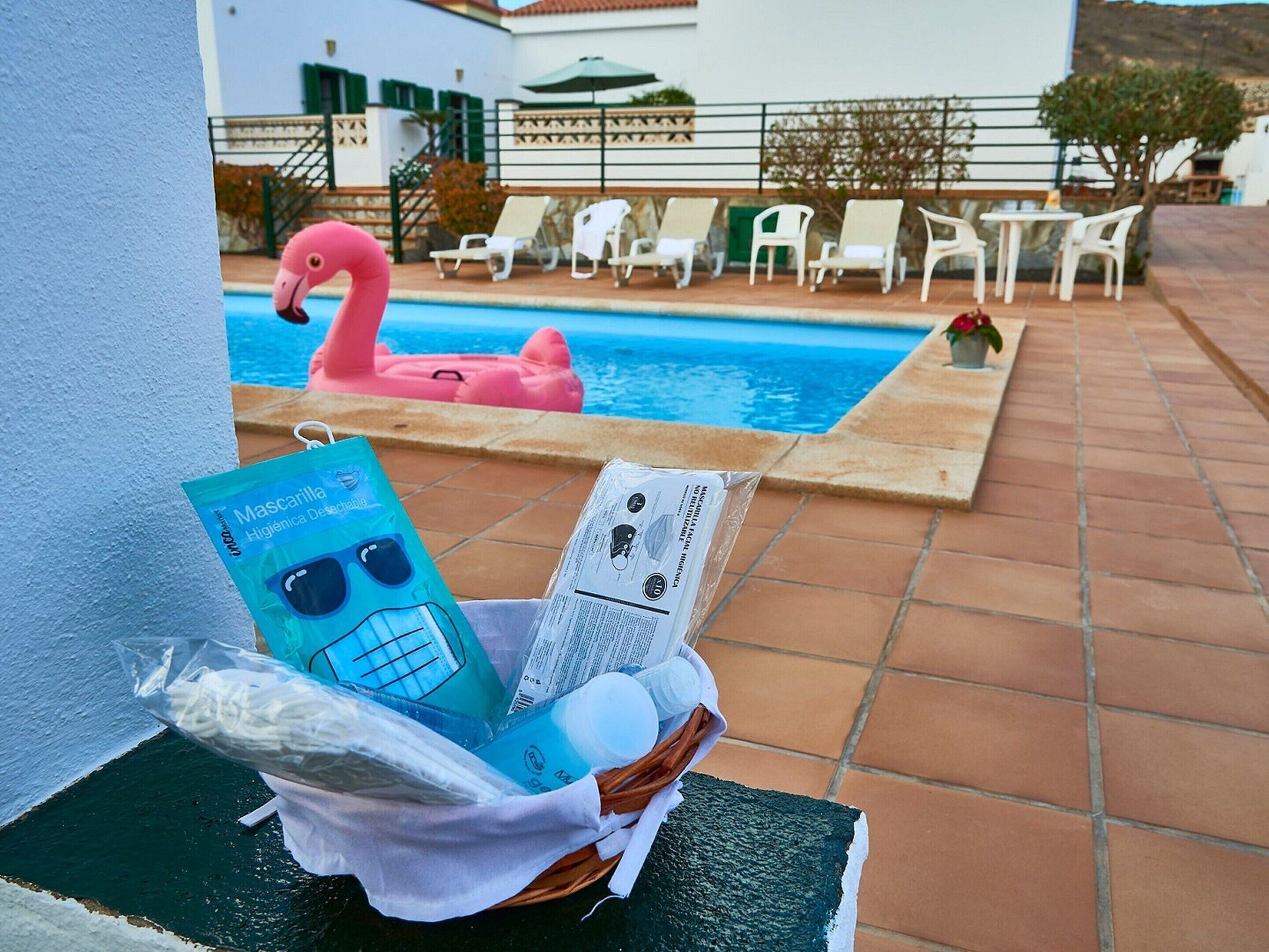 A poolside area with lounge chairs, a pink flamingo float, and a basket containing a blue package and a white bottle.
