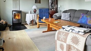 A cozy living room with a wood-burning stove, a blue armchair, a grey sofa, and a wooden coffee table. - 5 Person Holiday Home in Nexo (Nexø)