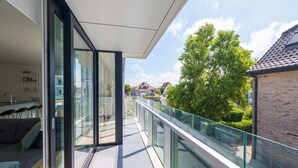 Een modern appartement met een glazen balkon, een keuken en uitzicht op omliggende huizen en bomen.