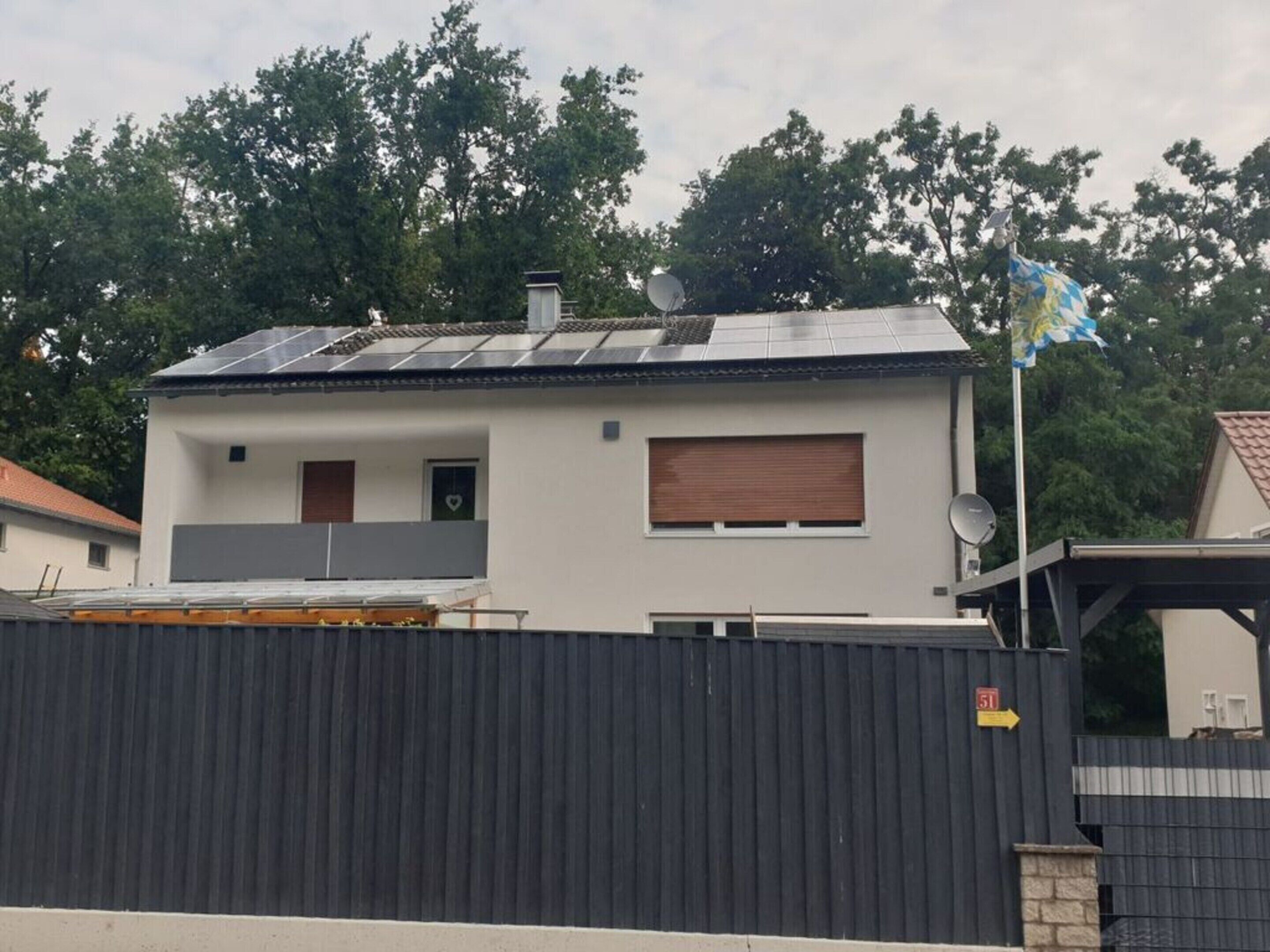 A modern two-story house with a solar panel roof, a satellite dish, and a flag.