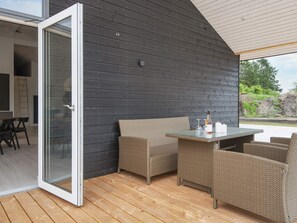 Um pátio externo com móveis de vime, uma mesa de vidro e vista para o exterior.