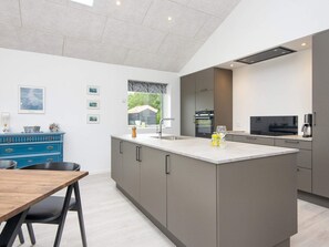 A modern kitchen with a central island, grey cabinetry, and a dining area with a wooden table and chairs. - 5 Star Holiday Home in Ansager (Ansager)