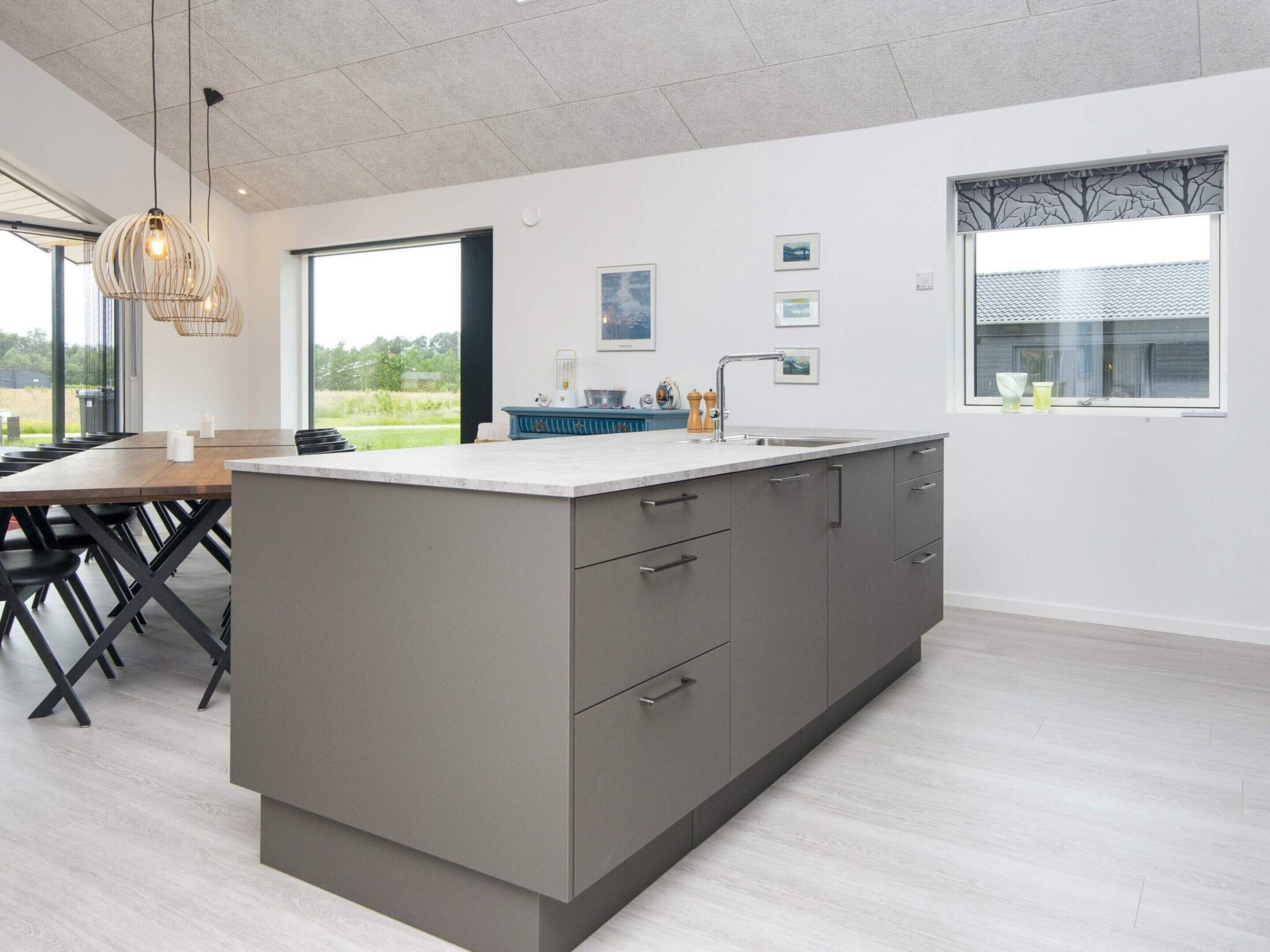 A modern kitchen with a large island, grey cabinetry, and a dining area with a wooden table and chairs.