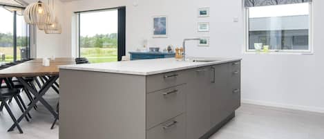 A modern kitchen with a large island, grey cabinetry, and a dining area with a wooden table and chairs.