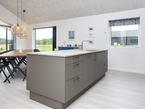 Cozinha moderna com uma ilha grande, armários cinza e vista para o exterior.