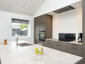 A modern kitchen with a built-in oven, a coffee machine, and a window with a view of a house. - 5 Star Holiday Home in Ansager (Ansager)