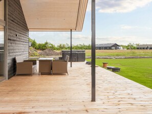 An outdoor deck with a table and chairs, a hot tub, and a grassy area. - 5 Star Holiday Home in Ansager (Ansager)