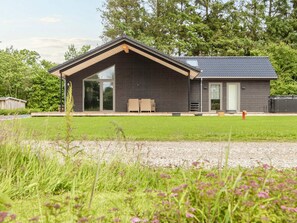 A modern building with a large glass door, a covered outdoor seating area, and a gravel driveway. - 5 Star Holiday Home in Ansager (Ansager)