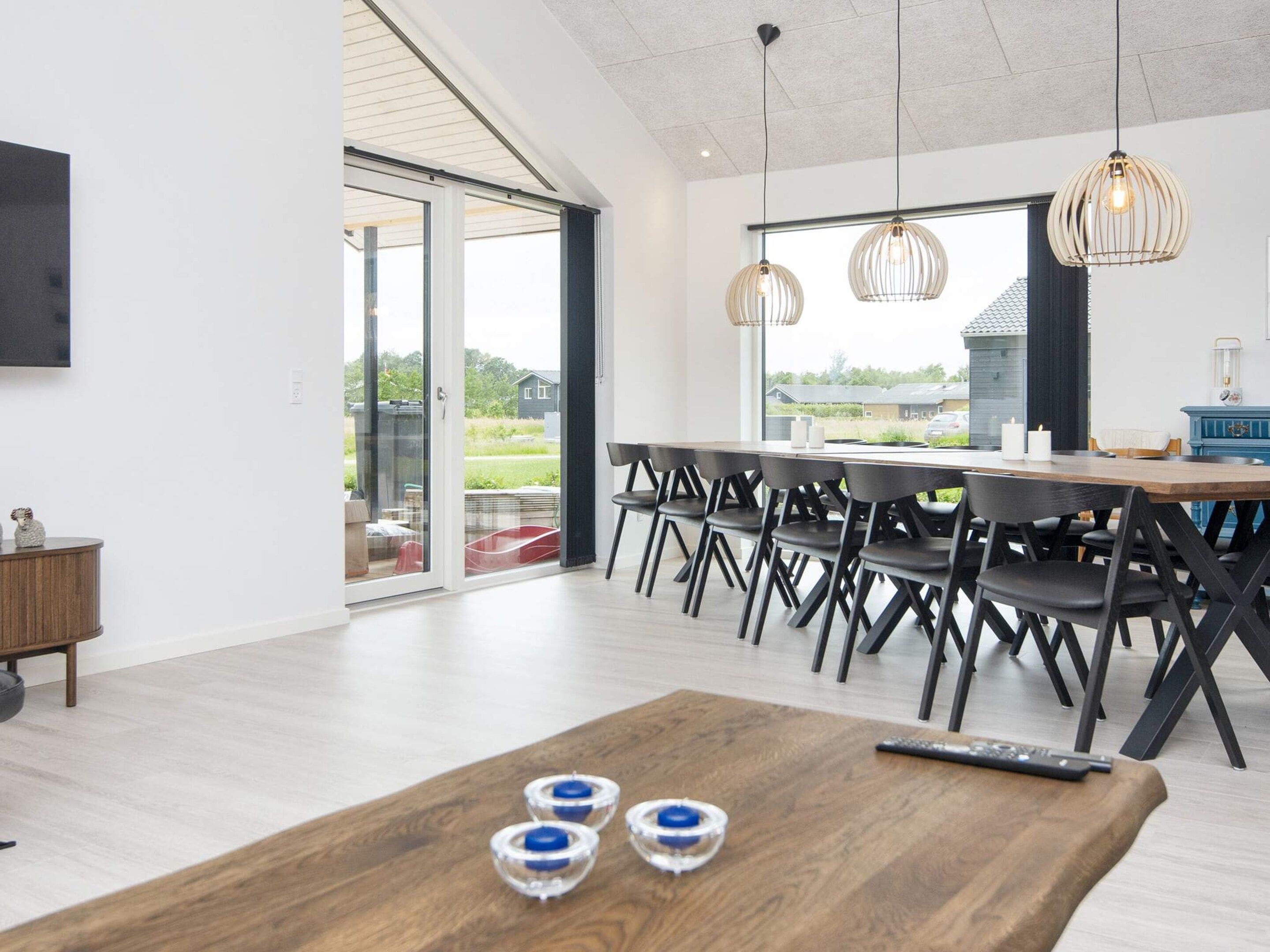 A modern dining area with a wooden table, black chairs, and pendant lighting.