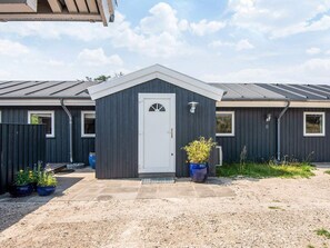 A modern building with a dark exterior, a white door, and a small porch area with potted plants. - 4 Star Holiday Home in Blokhus (Blokhus)