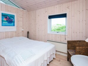 A bedroom with a large bed, a guitar, a wicker chair, and a window with a view of greenery. - 4 Star Holiday Home in Blokhus (Blokhus)