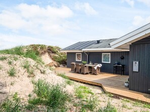 A modern house with a deck, a dining area with wicker furniture, and a dark exterior. - 4 Star Holiday Home in Blokhus (Blokhus)