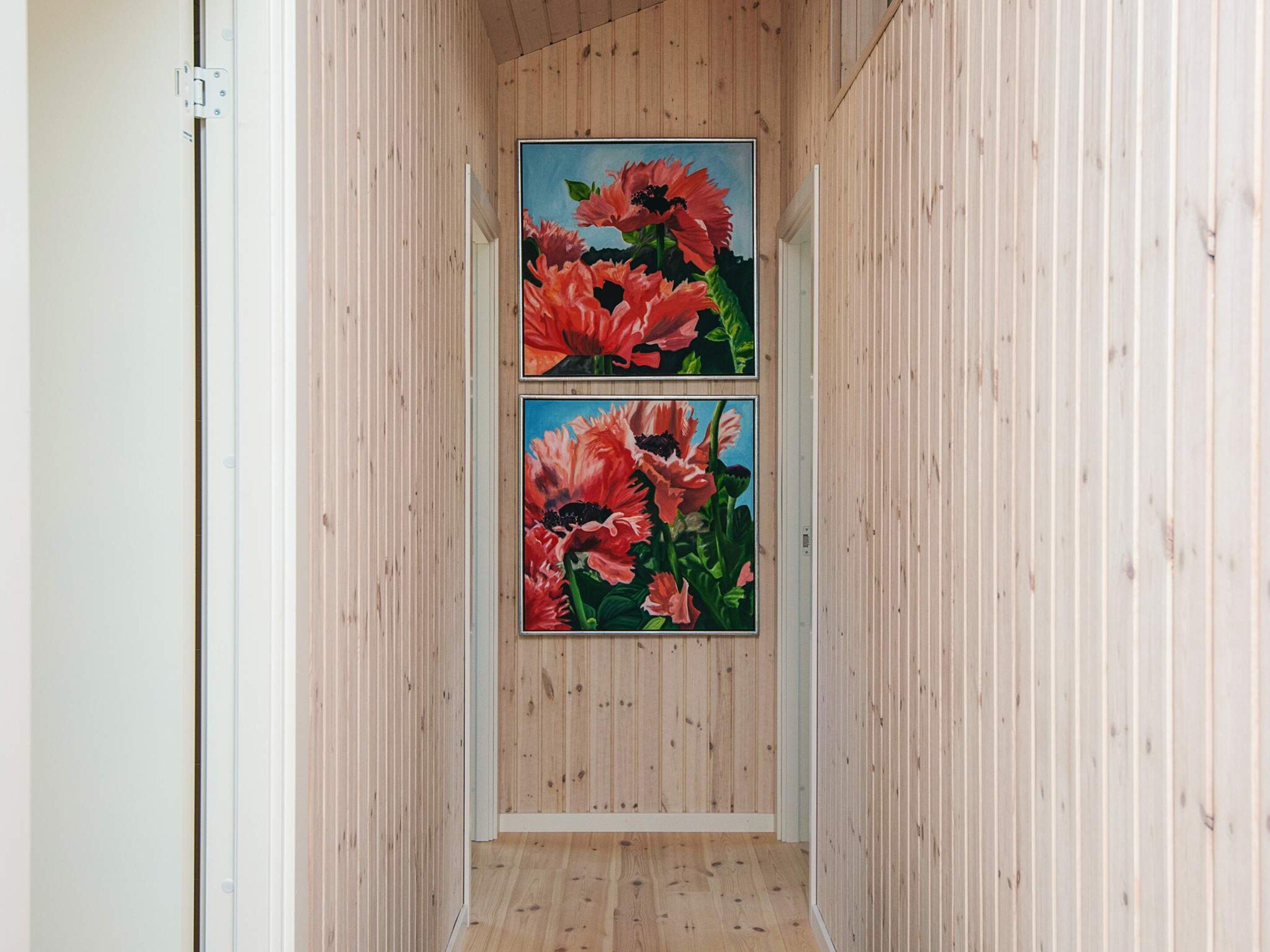 Un pasillo con paneles de madera y dos cuadros enmarcados con motivos florales en la pared.
