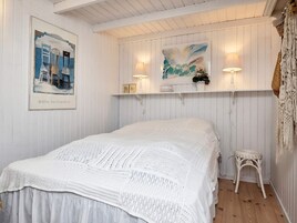 Un dormitorio con una cama grande, dos lámparas de pared, una obra de arte enmarcada y una silla blanca pequeña.