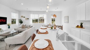 A modern kitchen with white cabinetry, a central island with a sink, and a dining area with a sofa and chairs.