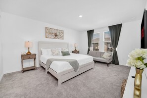Une chambre à coucher comprenant un lit, des tables de chevet, un canapé, une fenêtre avec des rideaux et un téléviseur fixé au mur.