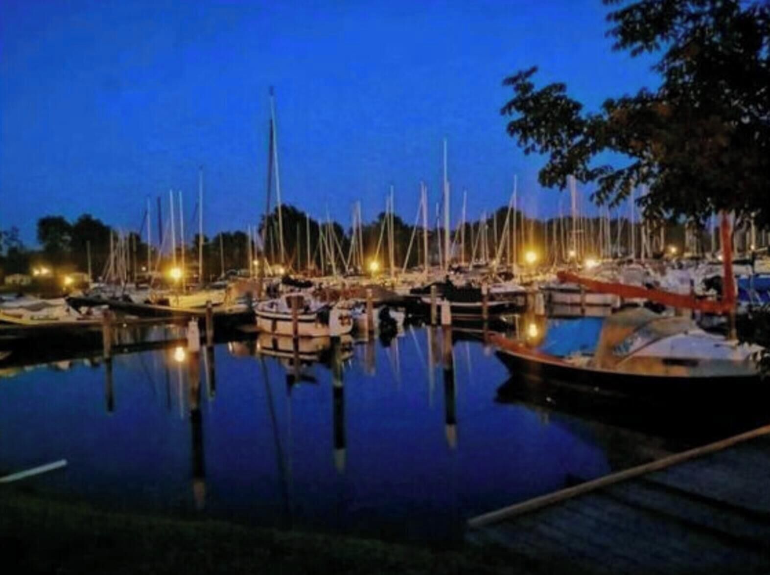 Ein Yachthafen im Abenddämmerung mit vertäuten Booten und Lichterreflexionen auf dem Wasser.