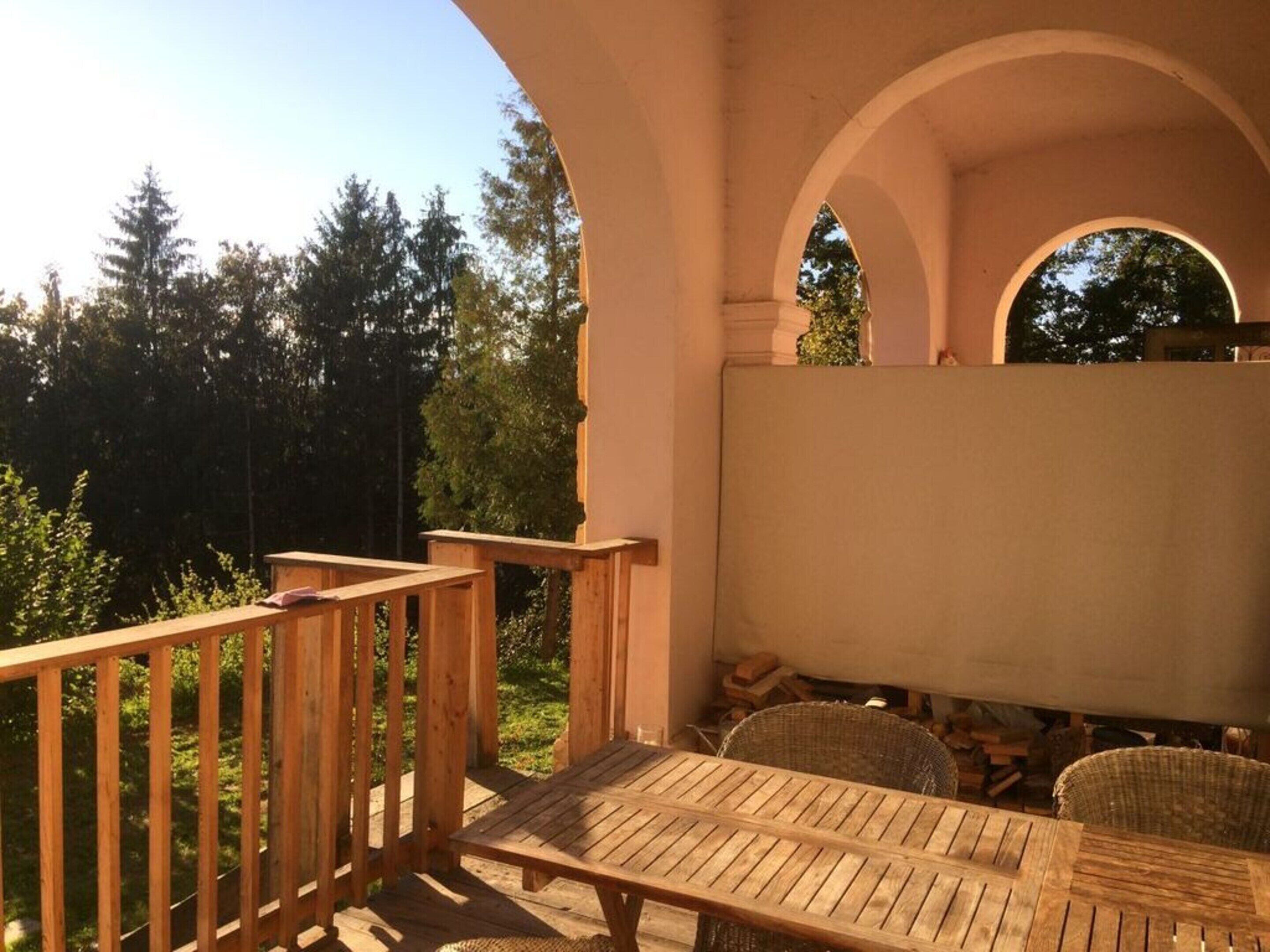 Un patio exterior con mobiliario de madera, una zona de estar cubierta y vistas a árboles.