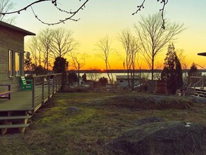 A wooden deck with a bench, a small shed, and a view of a sunset over a body of water.