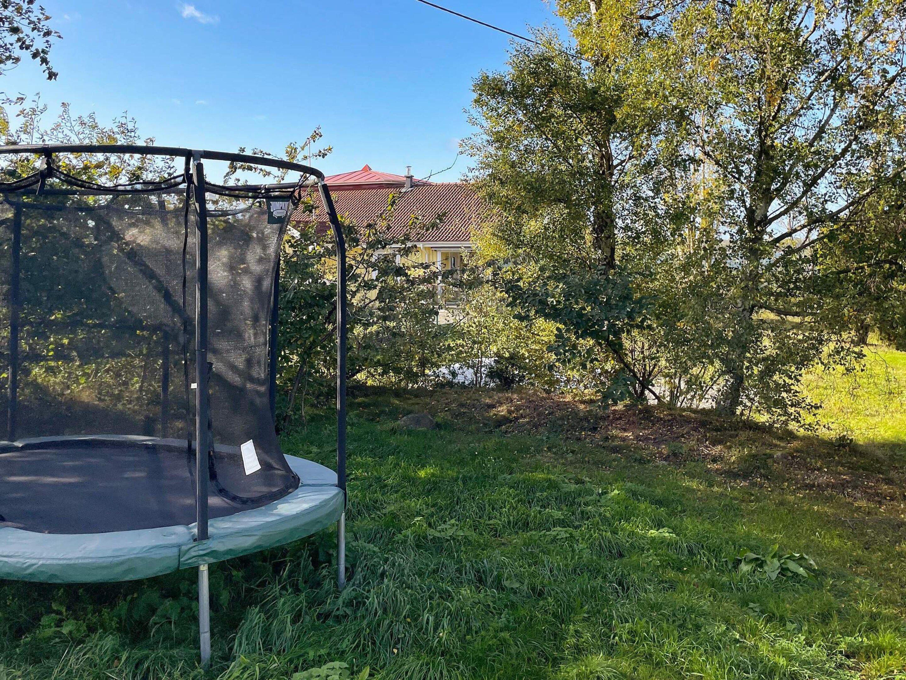A trampoline in a grassy yard with trees and a house in the background.