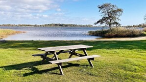 A picnic table in a grassy area with a lake and trees in the background. - 4 Star Holiday Home in Sturko (Sturkö)
