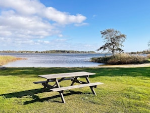 Una mesa de picnic en un área verde con un lago y árboles al fondo.