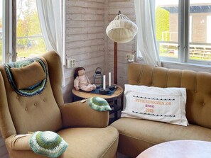 A cozy room with a wooden wall, a lamp, a small table with a candle, and a cushion with text.
