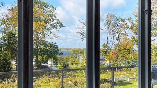 A view from a window overlooking a grassy deck with a metal railing, trees, and a body of water in the distance. - 4 Star Holiday Home in Sturko (Sturkö)