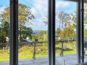 A view from a window overlooking a grassy deck with a metal railing, trees, and a body of water in the distance.