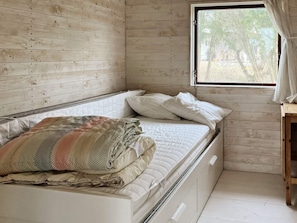 Uma cama de solteiro com colcha, janela com cortinas e parede de madeira.