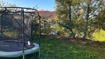 A trampoline in a grassy yard with trees and a building in the background.