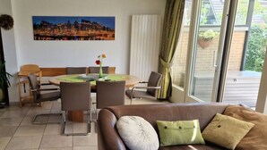 A modern living room with a brown leather sofa, a dining table with chairs, and a large window with curtains. - Sunshine Comfortable Holiday Residence (Sint Maarten)