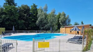 A swimming pool with lounge chairs and umbrellas, surrounded by a wooden fence and trees. - Sunshine Comfortable Holiday Residence (Sint Maarten)