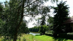 A grassy area with a path leading to a body of water, surrounded by trees and a building with a tiled roof. - Amazing Apartment in Templin (Templin)