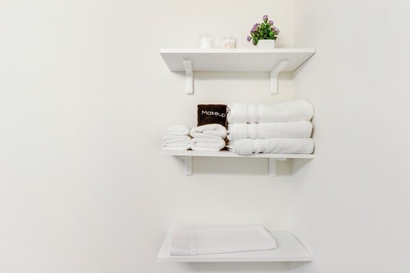 Un bagno con scaffali bianchi, asciugamani e una piccola pianta in vaso.