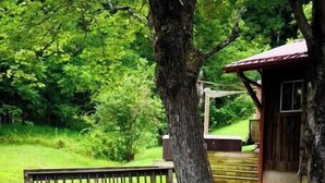 Un ponte di legno sopra un ruscello, circondato da vegetazione rigogliosa e un edificio rustico con tetto rosso.