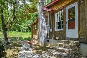 A rustic wooden building with a stone staircase leading to a door, surrounded by lush greenery.