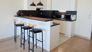 A modern kitchen with a central island, bar stools, and a coffee maker. - Couple Stay Near Beaches (Nieuwpoort)