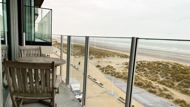 A balcony with a view of the beach, a wooden chair, and a table. - Couple Stay Near Beaches (Nieuwpoort)