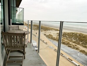 Un balcon avec vue sur la plage, une chaise en bois et une table.