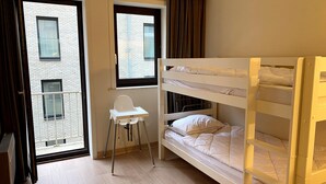 A room with a bunk bed, a small desk, and a window with a view of a building. - Couple Stay Near Beaches (Nieuwpoort)