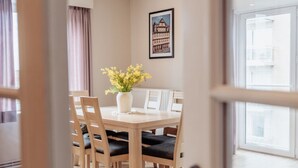 A dining area with a wooden table and chairs, a vase with yellow flowers, and a framed picture on the wall. - Goethe 0202 Furnished Apartment With sea View (De Haan)