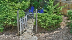 Un chemin de pierres menant à une porte en bois, entouré d’un feuillage verdoyant et dense et d’une clôture en bois.