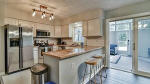 Une cuisine moderne dotée d’appareils électroménagers en acier inoxydable, d’un îlot central en bois et d’une porte-fenêtre coulissante donnant sur une terrasse.