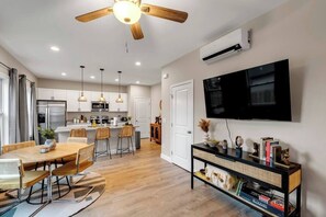 A modern kitchen with a dining area, a ceiling fan, and a mounted TV.