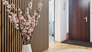 A hallway with a wooden slat wall, a white vase with pink flowers, a wooden floor, a white rug, a door, and a clock on the wall. - "Sweet Home" (Central & Quiet) **** (München)