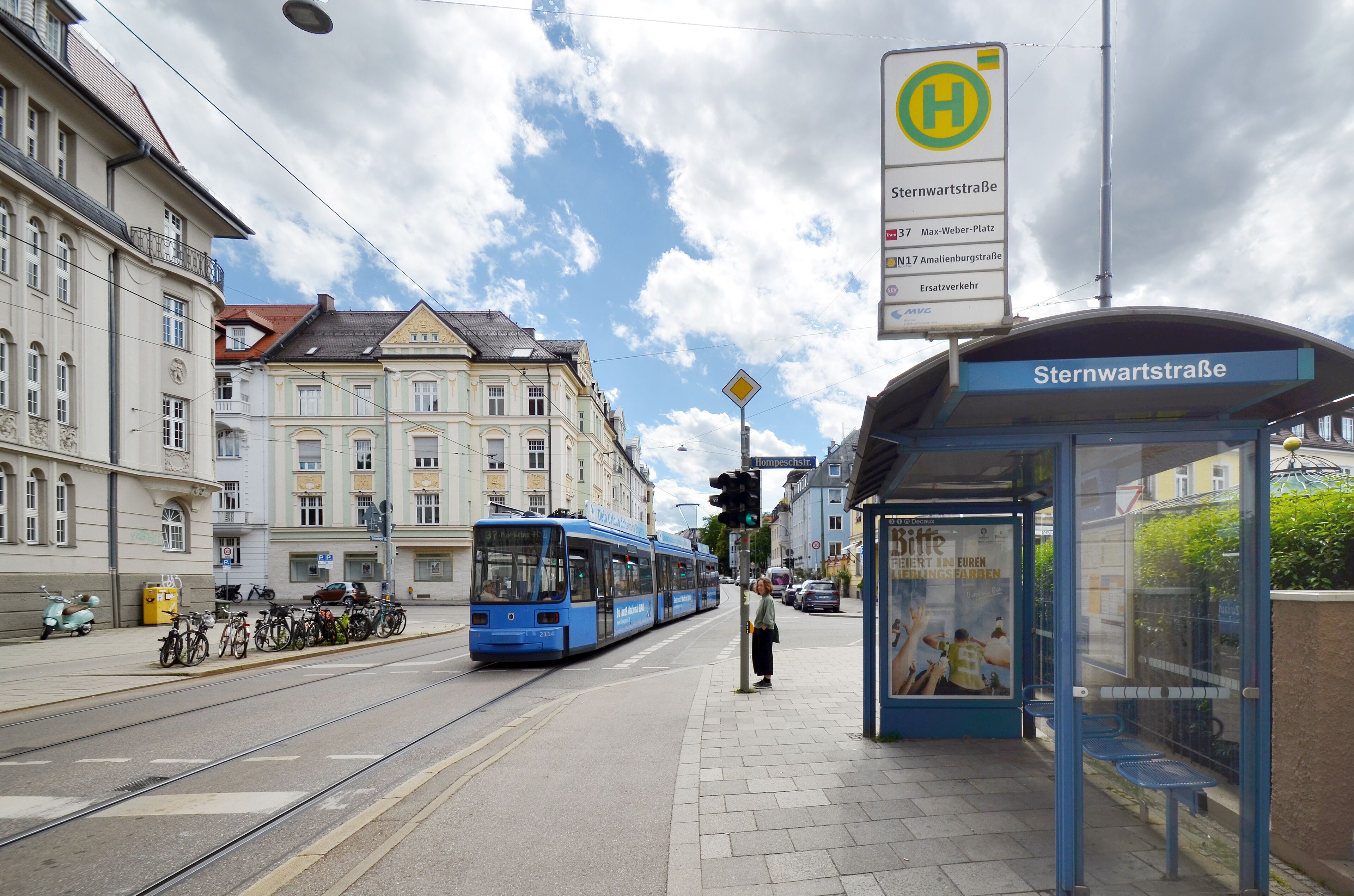 Een tram op een station, met een heldere lucht en gebouwen op de achtergrond.