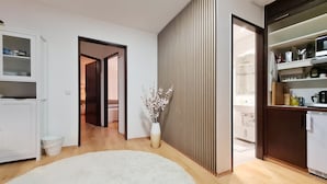 A modern living room with a white sofa, a wooden floor, a white rug, a vase with flowers, and a kitchen area with cabinets and appliances. - "Sweet Home" (Central & Quiet) **** (München)